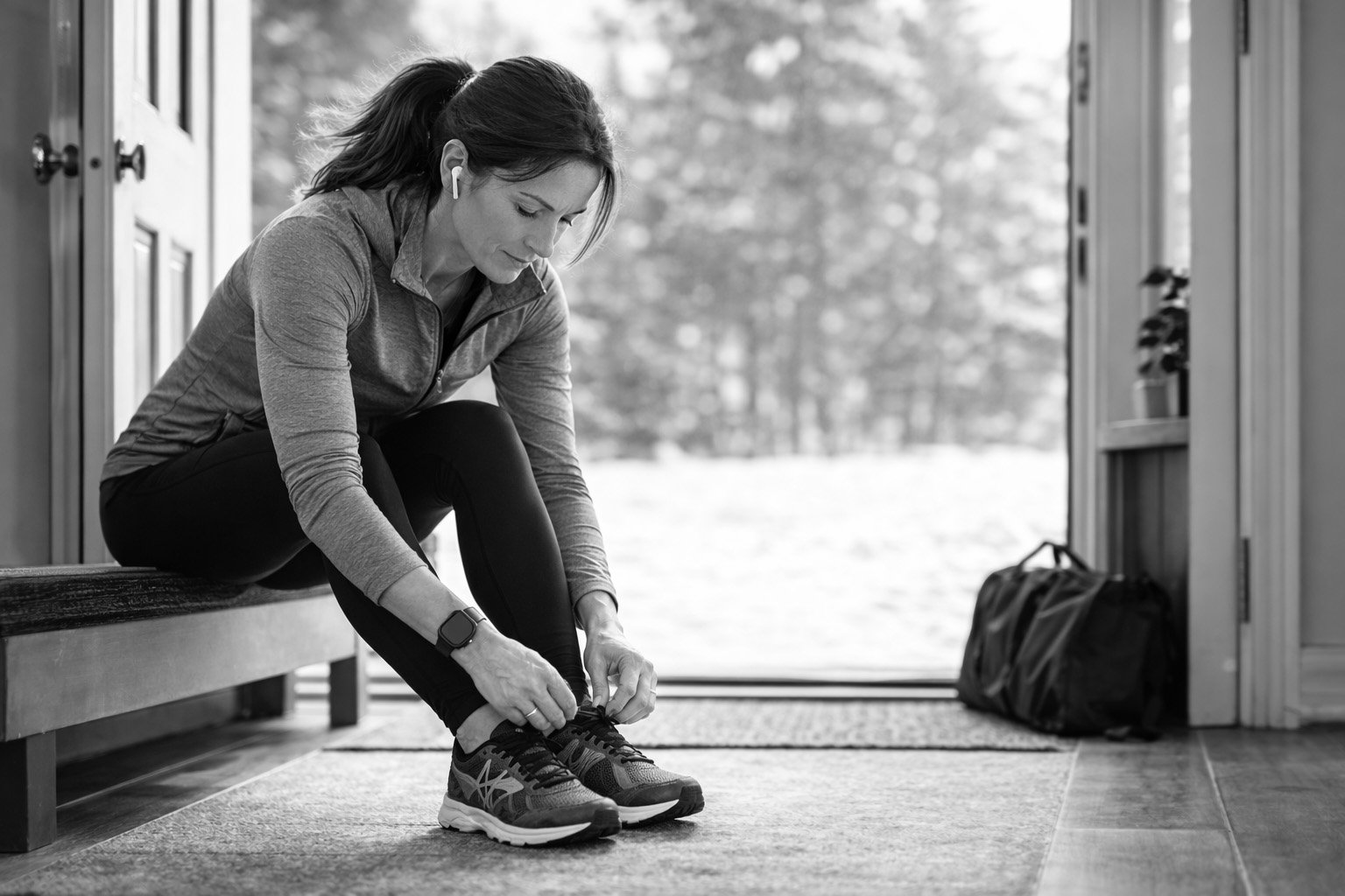 Middle-aged woman tying her running shoes by the door, representing momentum, daily movement, and consistent fitness after 45